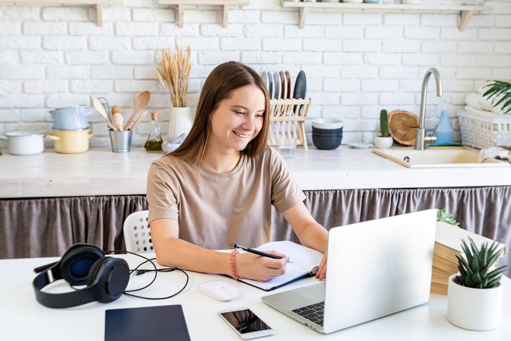 Distance learning. Teenager girl studying using the laptop at home kitchen