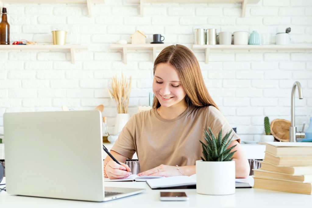 Teen girl smiling doing homework studying from home, distance learning, e-learning