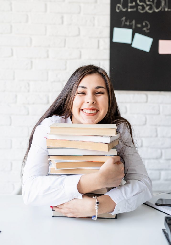 Young teacher sitting with pile of books looking away ready for lesson